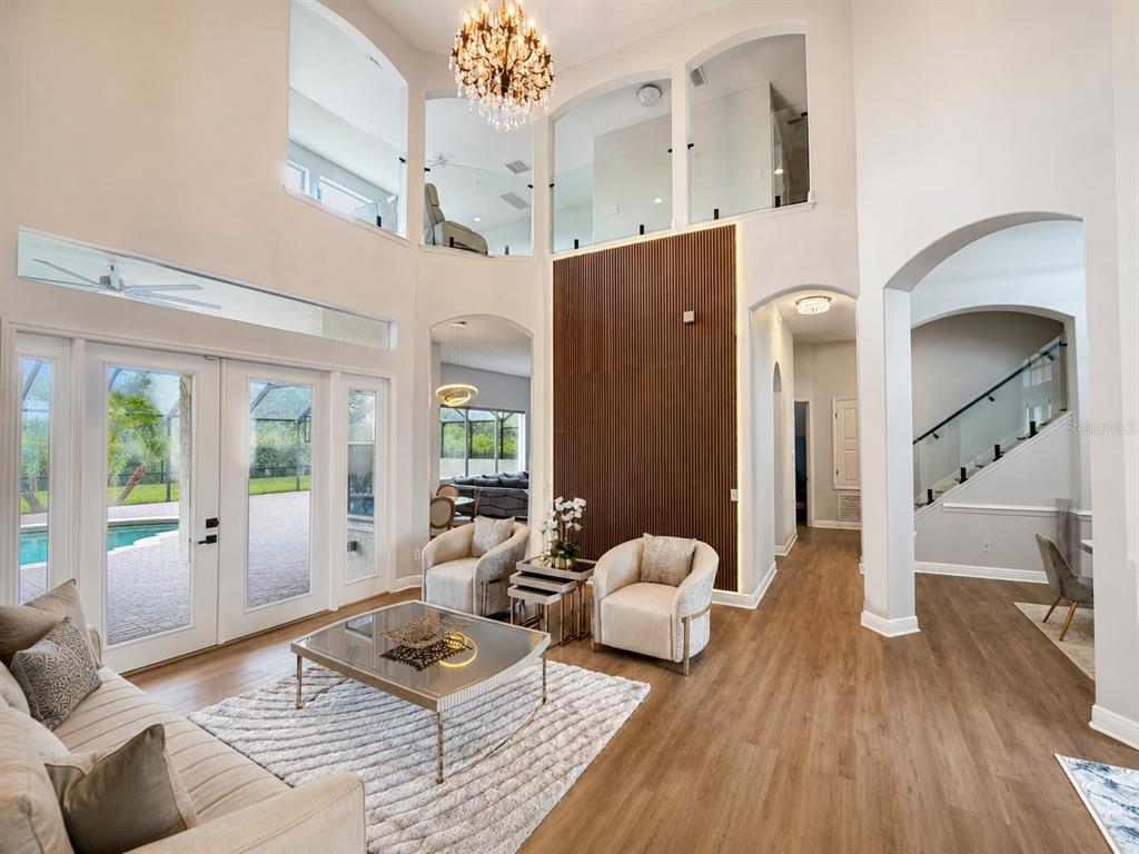 A two-story living room features a wood-slat accent wall, chandelier, and glass-railed upper balcony — 8412 DUNHAM STATION DRIVE, TAMPA, FL