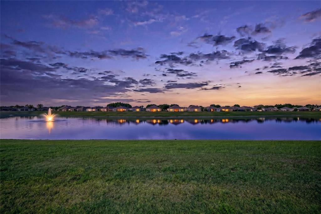 A pond with a fountain reflects a row of houses under a sunset sky — 9186 SW 70TH LOOP, OCALA, FL