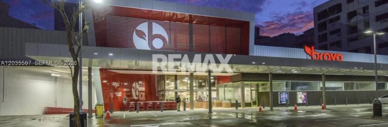 The exterior of a modern commercial building features a large Bravo supermarket entrance at dusk — 1 terreno # 1, FL