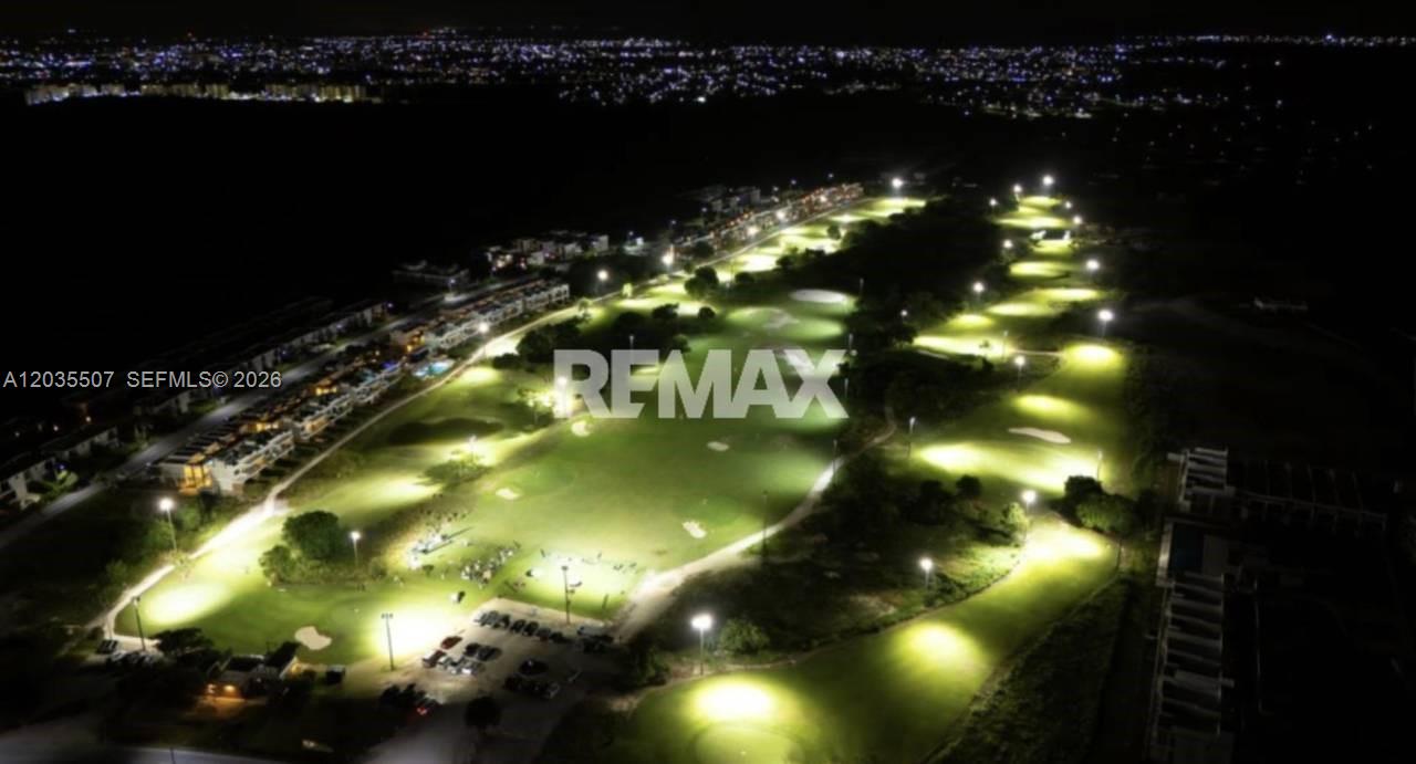 An aerial night view shows a brightly lit golf course adjacent to residential buildings — 1 terreno # 1, FL