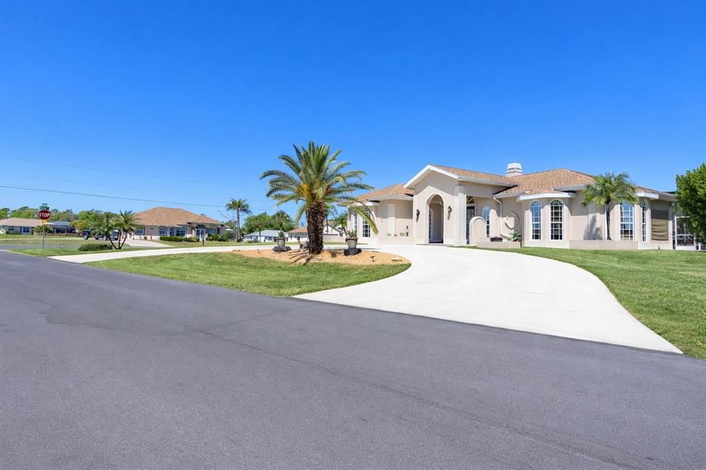 A beige single-story house with a circular driveway and palm trees under a clear sky — 2 LONG MEADOW ROAD, ROTONDA WEST, FL