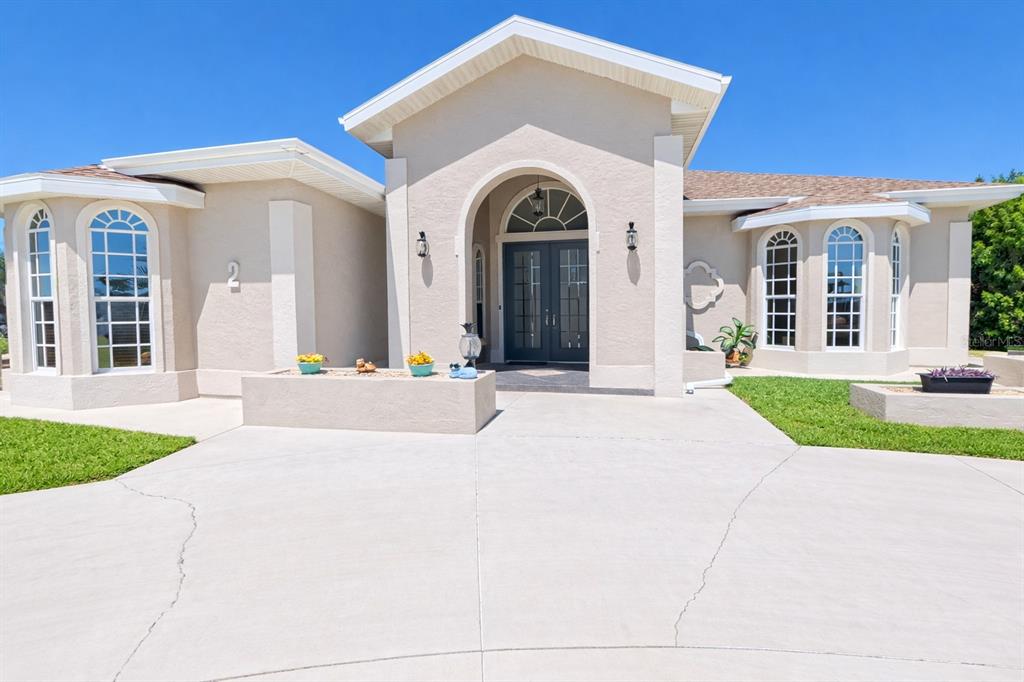 A beige single-story house features a prominent arched entryway and a concrete driveway — 2 LONG MEADOW ROAD, ROTONDA WEST, FL