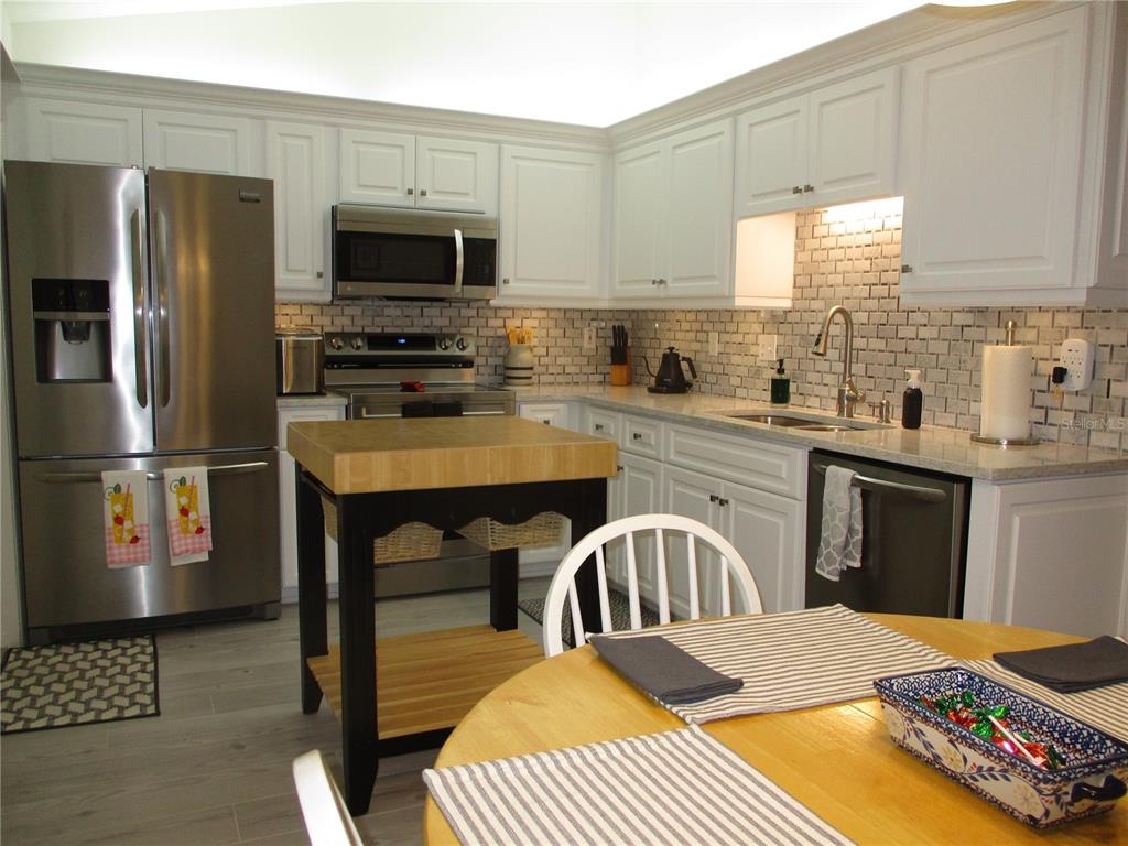 A kitchen with white cabinets, stainless steel appliances, a subway tile backsplash, and a wooden island — 11653 SW 138TH LANE, DUNNELLON, FL