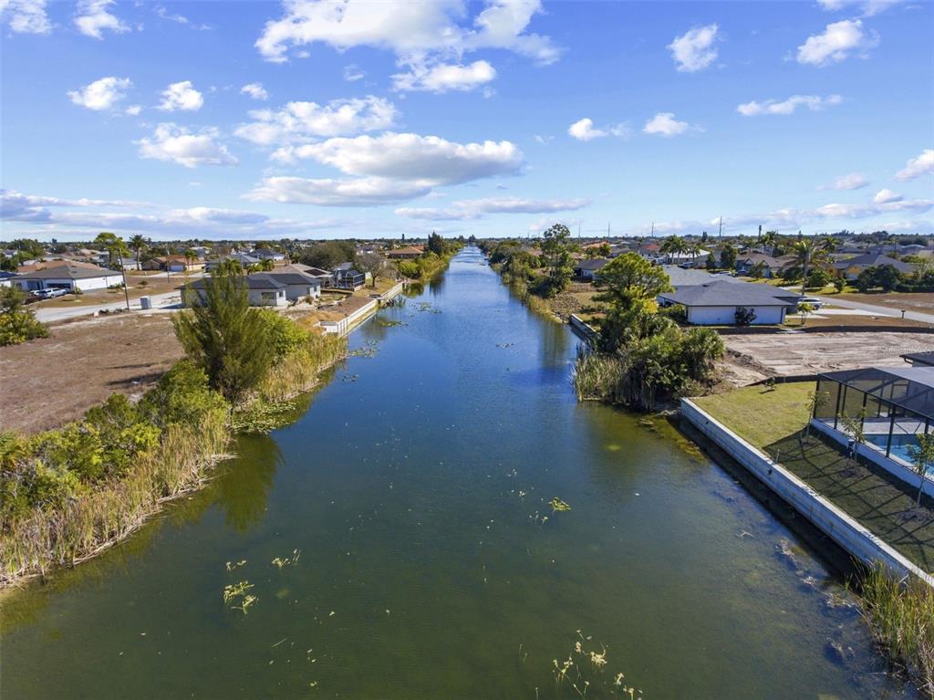 An aerial view of a canal flowing between residential properties under a partly cloudy sky — 704 NW 9TH STREET, CAPE CORAL, FL