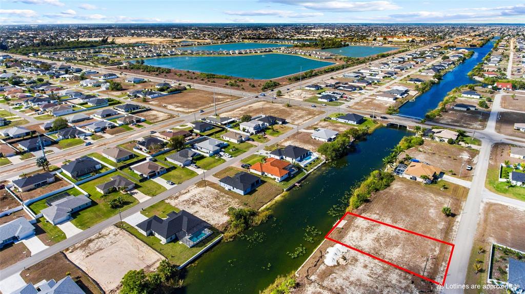 An aerial view shows a vacant residential lot outlined in red next to a canal — 704 NW 9TH STREET, CAPE CORAL, FL