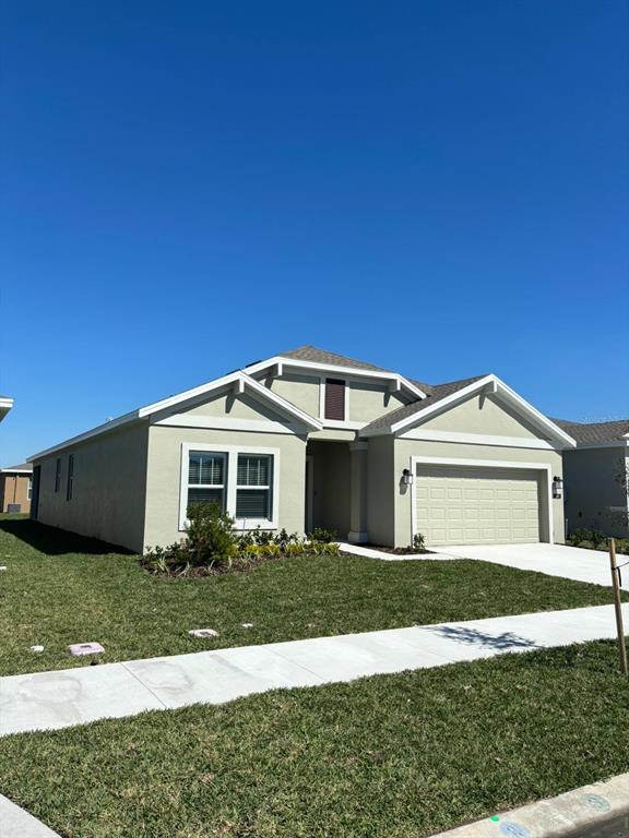 A single-story house with light green stucco siding, a two-car garage, and a front lawn — 541 HATTERAS ROAD, DAVENPORT, FL