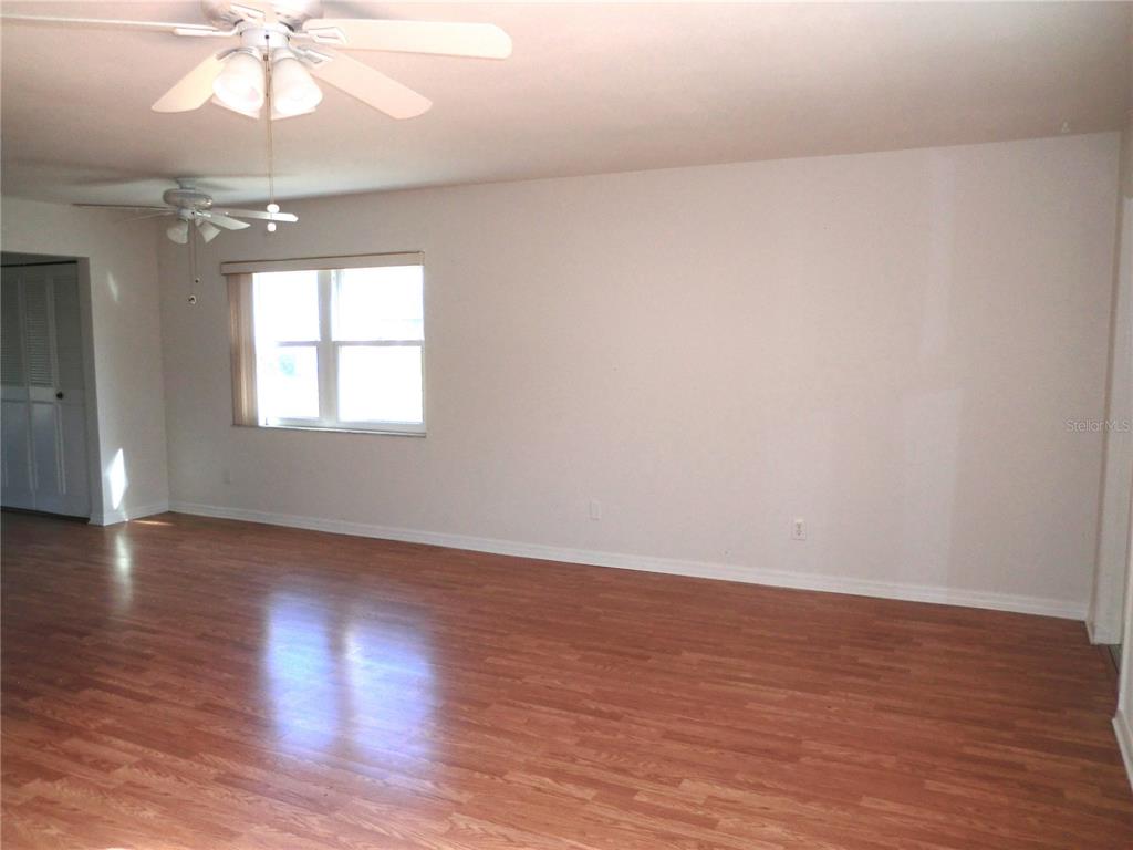 An empty room features wood-look laminate flooring, white walls, and two ceiling fans — 1902 ANDOVER STREET UNIT 203, SUN CITY CENTER, FL