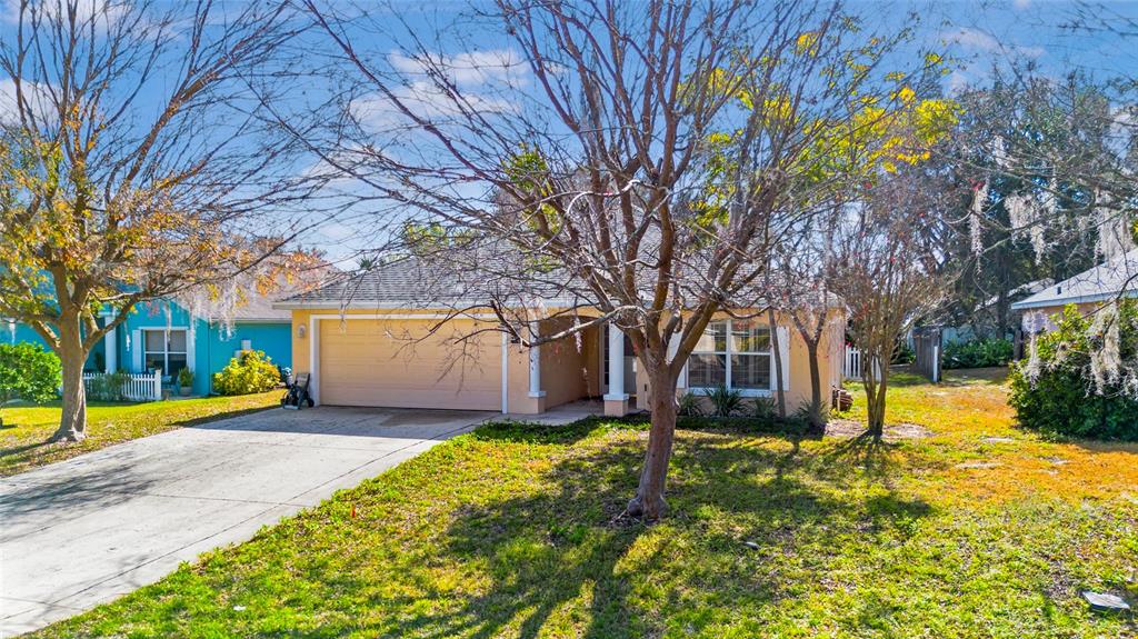 A single-story tan house with a two-car garage and a front yard with trees — 10314 PATRICK DRIVE, LEESBURG, FL