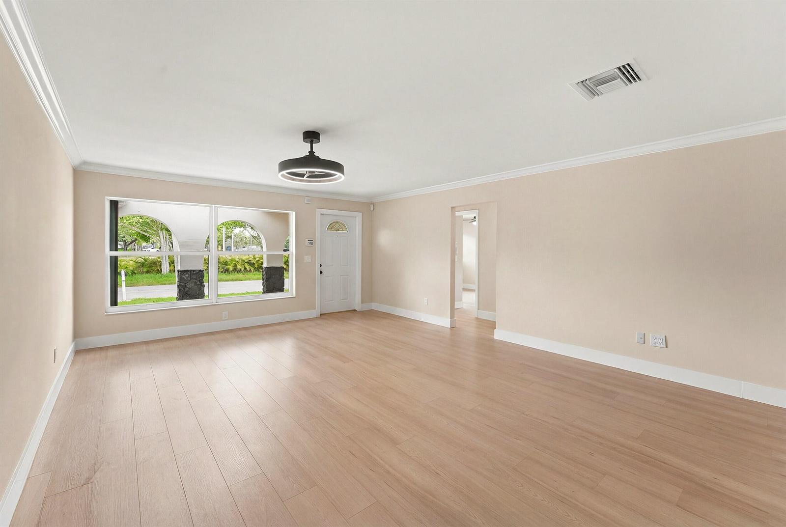 An empty living room features light wood flooring, beige walls, a ceiling fan, and windows — 22267 SW 57th Avenue, Boca Raton FL 33428, BOCA RATON, FL