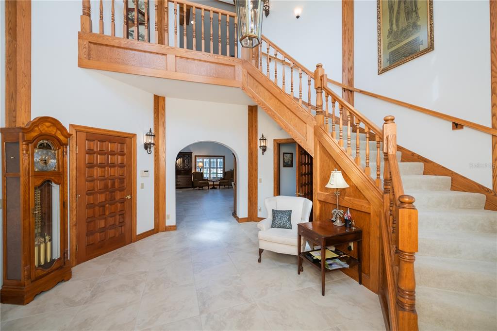 A grand foyer features a wooden staircase, tiled floors, a grandfather clock, and arched entryways — 5019 BAL HARBOR BOULEVARD, PUNTA GORDA, FL