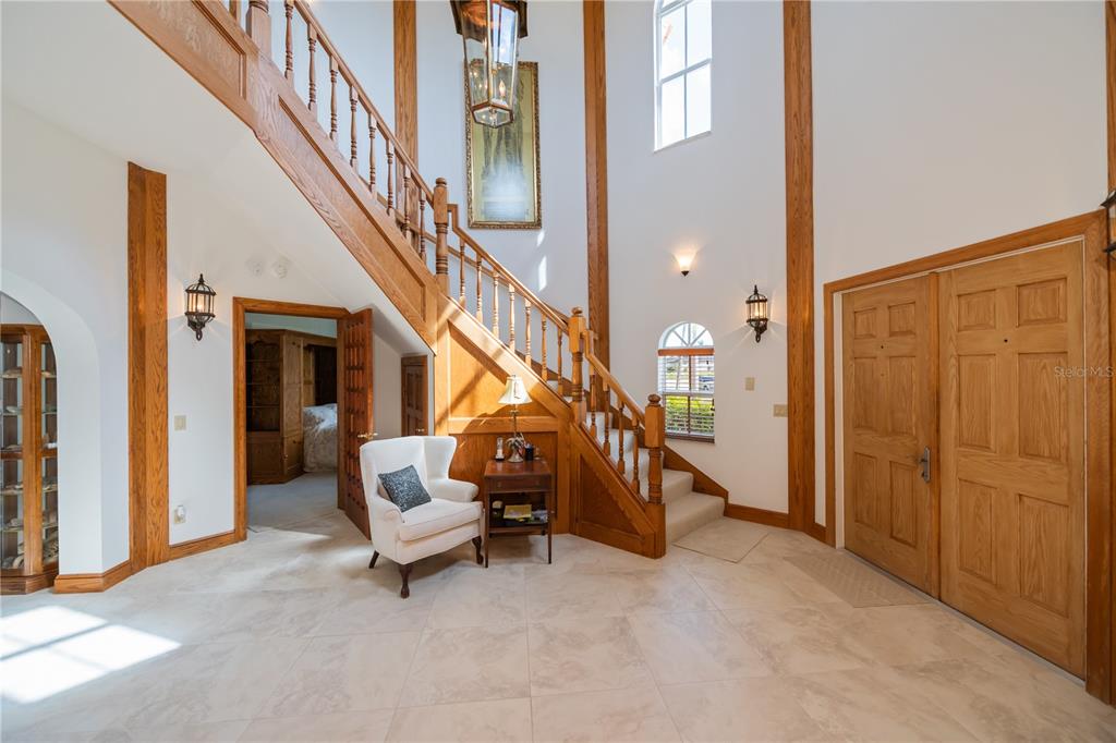A grand foyer features a wooden staircase, tile flooring, and a white armchair — 5019 BAL HARBOR BOULEVARD, PUNTA GORDA, FL