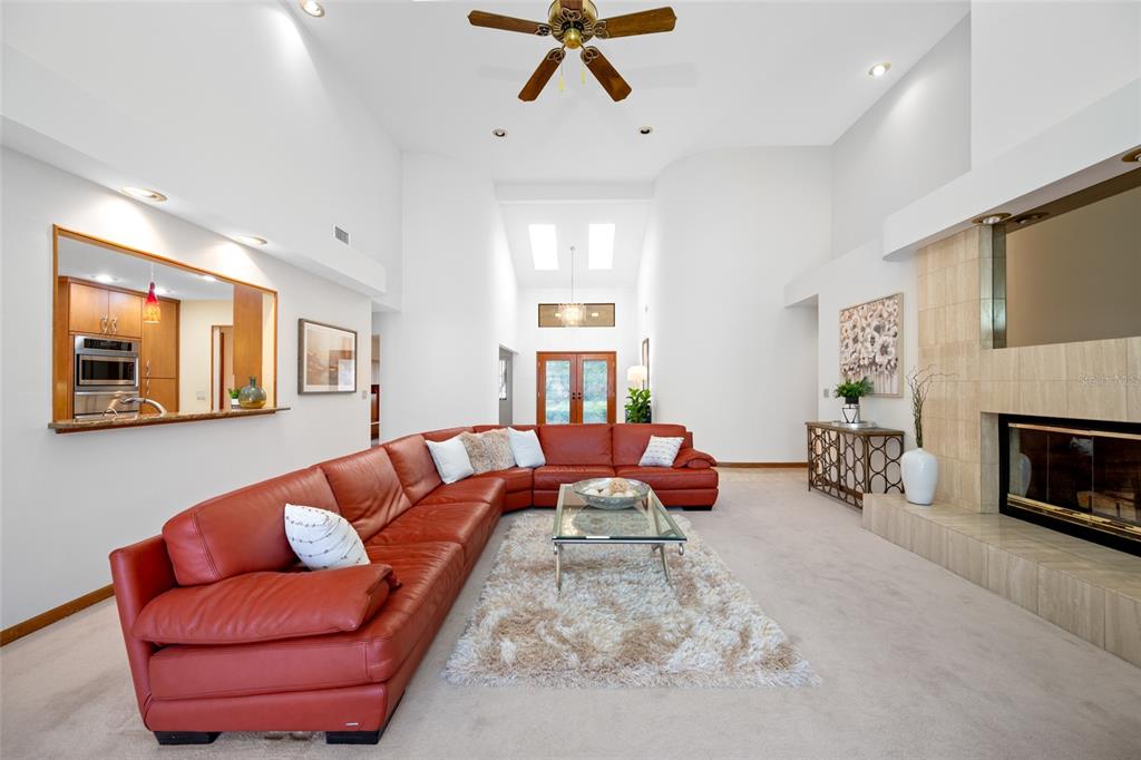 A spacious living room features a red sectional sofa, vaulted ceilings, skylights, and pool views — 9807 COMPASS POINT WAY, TAMPA, FL