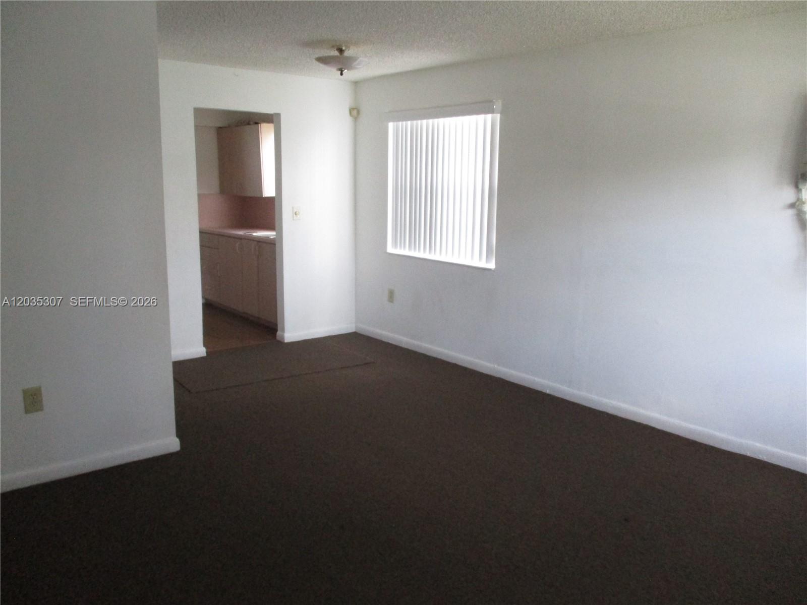 A room with brown carpeting and white walls features a window and a kitchen doorway — 10622 SW 174th Ter # 10622, Miami FL 33157, MIAMI, FL