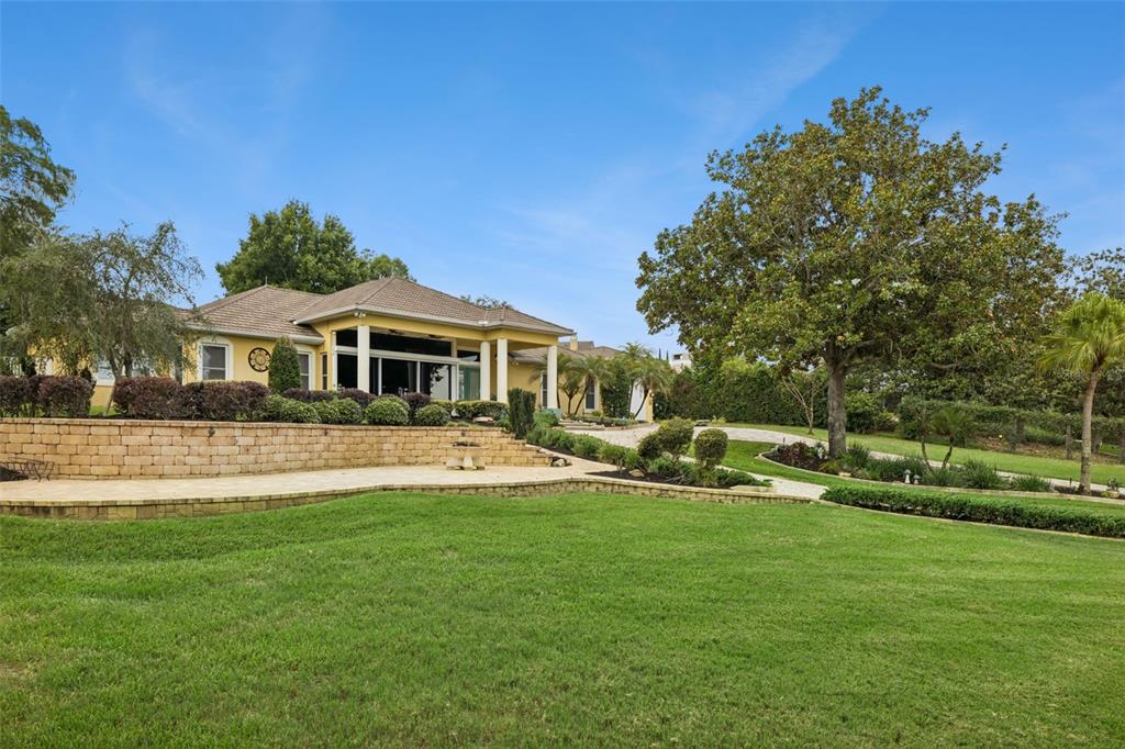 A large yellow house with a stone retaining wall overlooks a spacious green lawn — 12128 LAKESHORE DRIVE, CLERMONT, FL