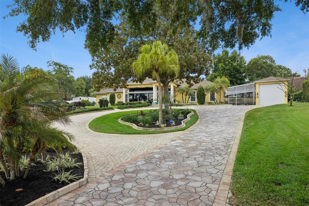A yellow house features a circular stone driveway and a detached garage — 12128 LAKESHORE DRIVE, CLERMONT, FL