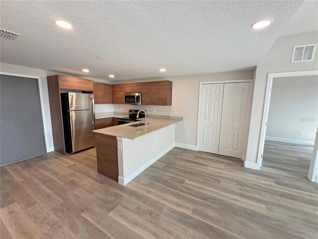 A kitchen features wood-tone cabinets, stainless steel appliances, and a peninsula with a stone countertop — 4424 S TEXAS AVENUE UNIT 1-320, ORLANDO, FL