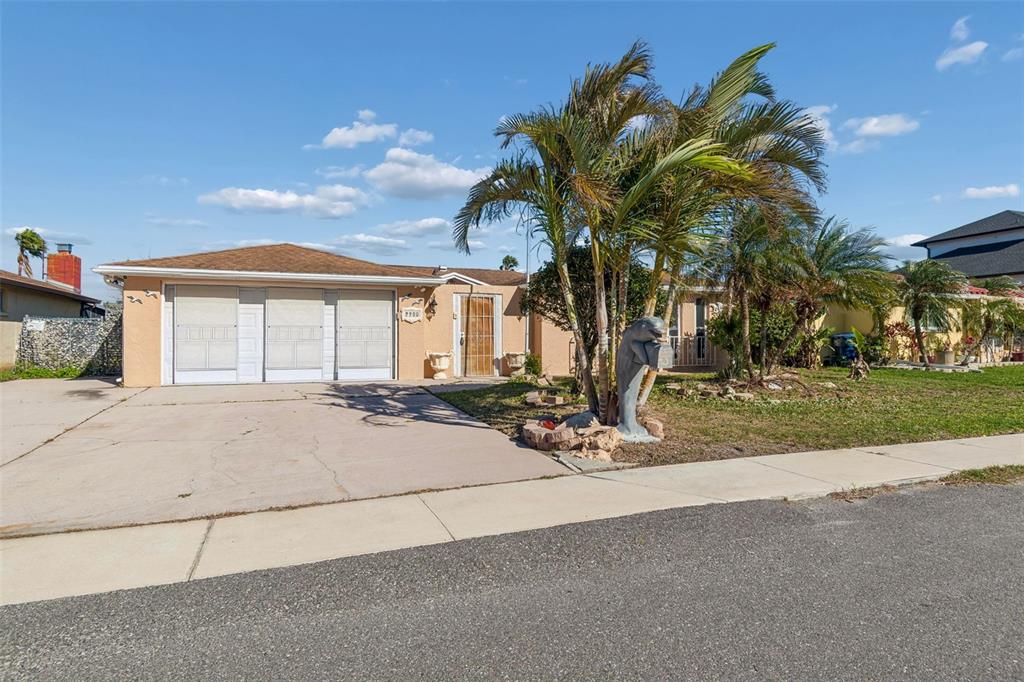 A single-story house with a beige stucco exterior, a three-car garage, and a palm tree — 9900 ISLAND HARBOR DRIVE, PORT RICHEY, FL