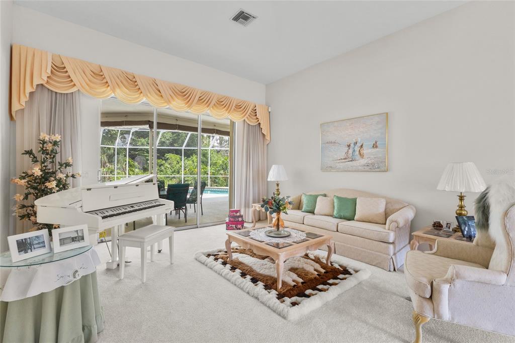 A living room features a white grand piano, a beige sofa, and sliding glass doors — 832 CARNOUSTIE DRIVE, VENICE, FL