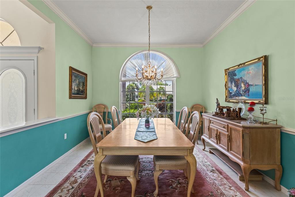 A dining room with a wooden table, chandelier, and two-toned green and teal walls — 832 CARNOUSTIE DRIVE, VENICE, FL