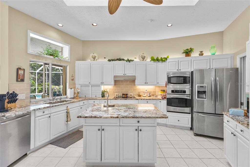 A kitchen with white cabinets, granite countertops, a central island, and stainless steel appliances — 832 CARNOUSTIE DRIVE, VENICE, FL