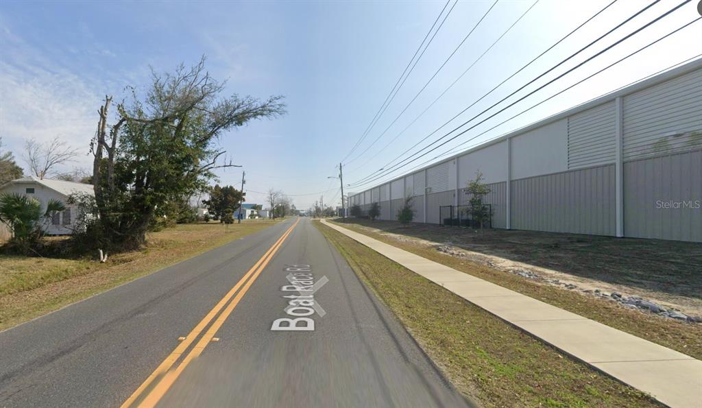 A paved road with a sidewalk runs between a residential house and a large warehouse — 5321 BOAT RACE ROAD, PANAMA CITY, FL