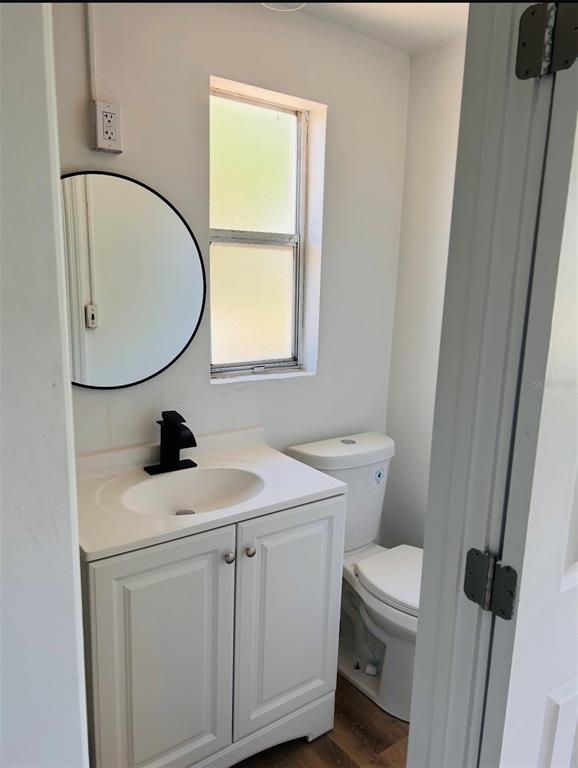 A small bathroom features a white vanity, a round mirror, and a toilet — 2214 Ave B SW SW 2214 AVE B SW, WINTER HAVEN, FL