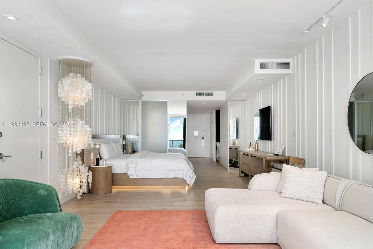 A modern bedroom and living area features a white bed, green chair, and coral rug — 2201 Collins Ave # 532, Miami Beach FL 33139, MIAMI BEACH, FL