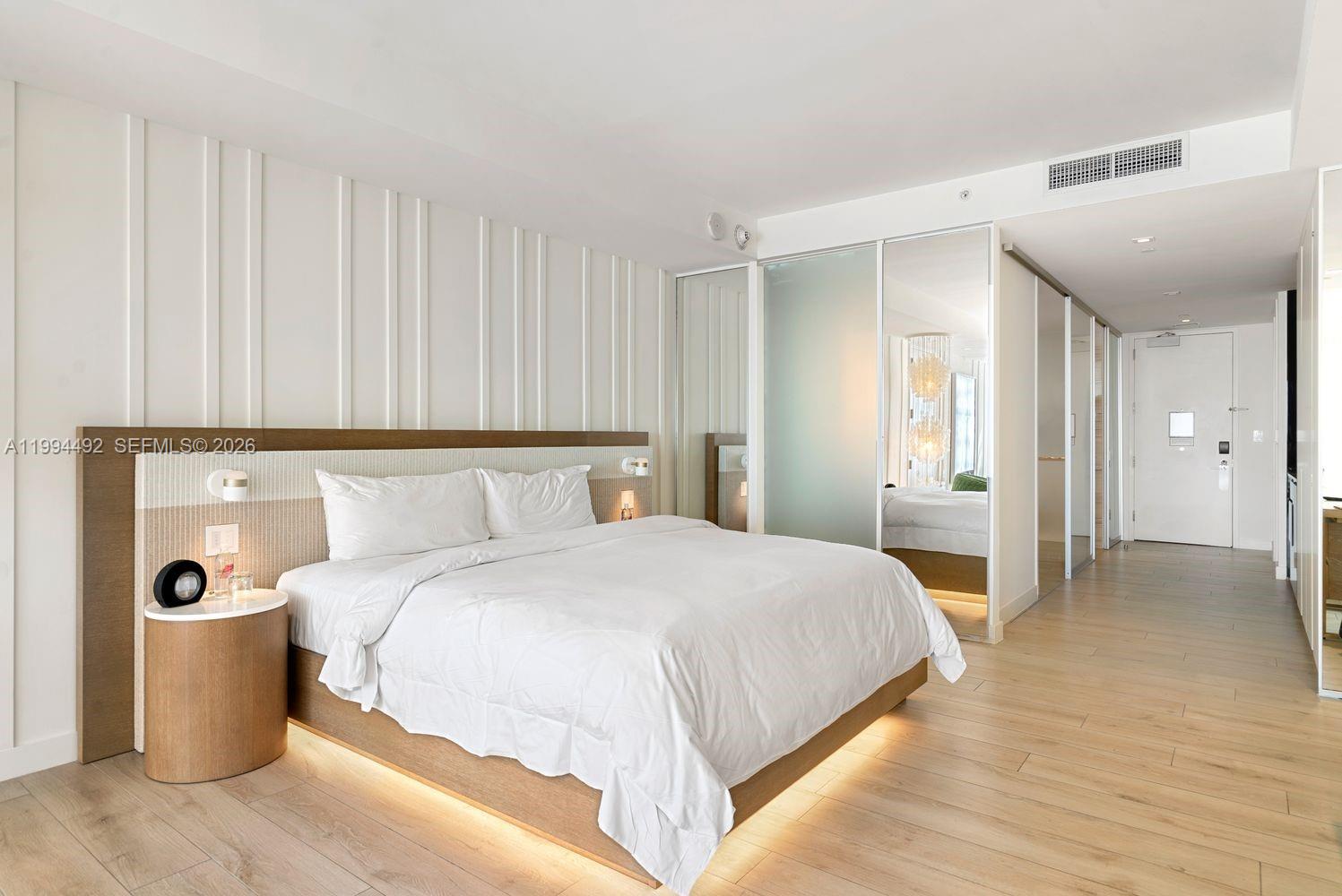 A modern bedroom features a platform bed, light wood flooring, and mirrored sliding closet doors — 2201 Collins Ave # 532, Miami Beach FL 33139, MIAMI BEACH, FL