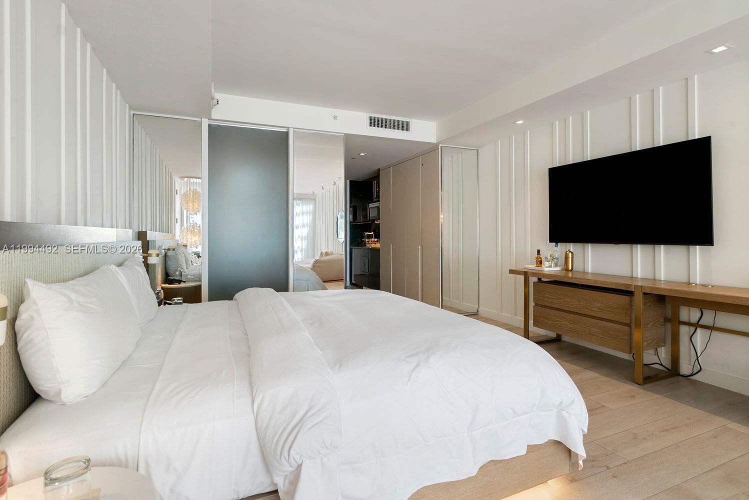 A modern bedroom features a large bed, a wall-mounted television, and light wood flooring — 2201 Collins Ave # 532, Miami Beach FL 33139, MIAMI BEACH, FL