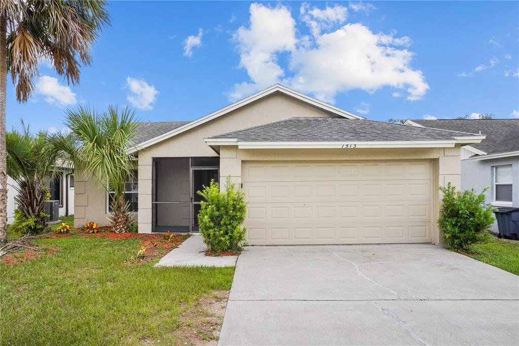 A single-story house with a beige stucco exterior, a two-car garage, and a screened entryway — 1513 INDIAN OAKS TRAIL, KISSIMMEE, FL