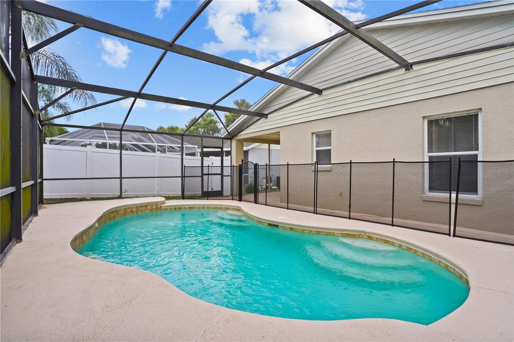 A backyard swimming pool is enclosed by a screened lanai and a black safety fence — 1513 INDIAN OAKS TRAIL, KISSIMMEE, FL