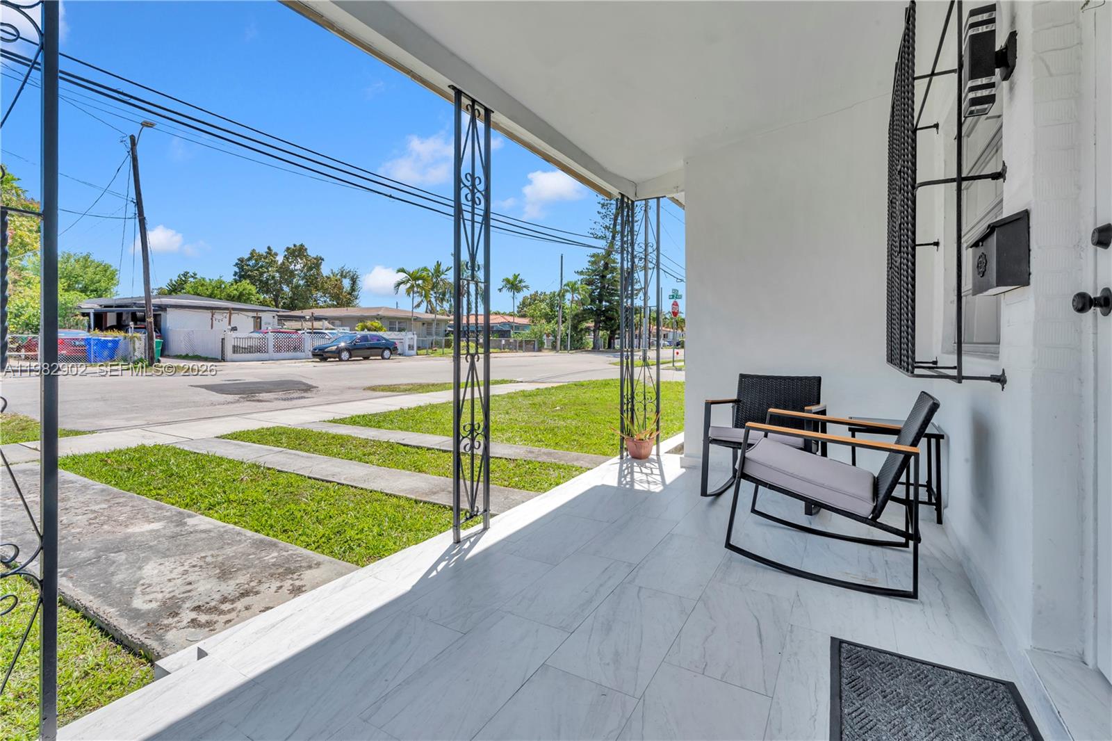 A covered front porch features white tiled flooring, metal support columns, and two rocking chairs — 250 NW 34th Ave, Miami FL 33125, MIAMI, FL