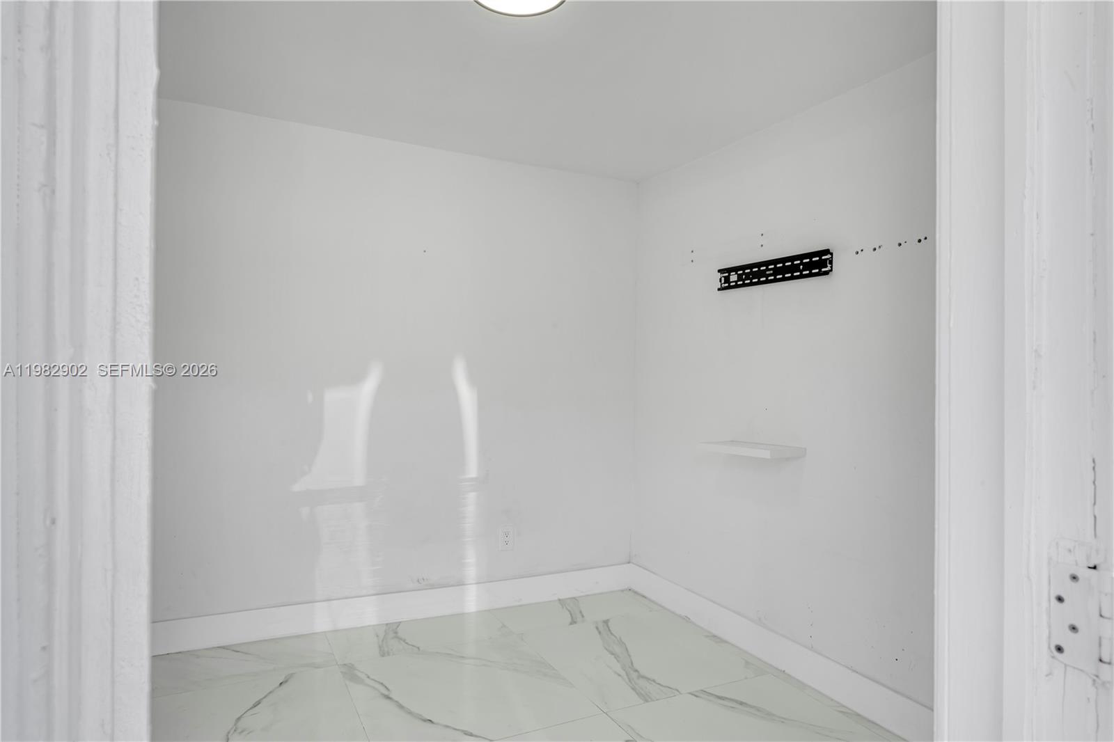 A small, empty room features white walls, marble-patterned tile flooring, and a wall-mounted television bracket — 250 NW 34th Ave, Miami FL 33125, MIAMI, FL