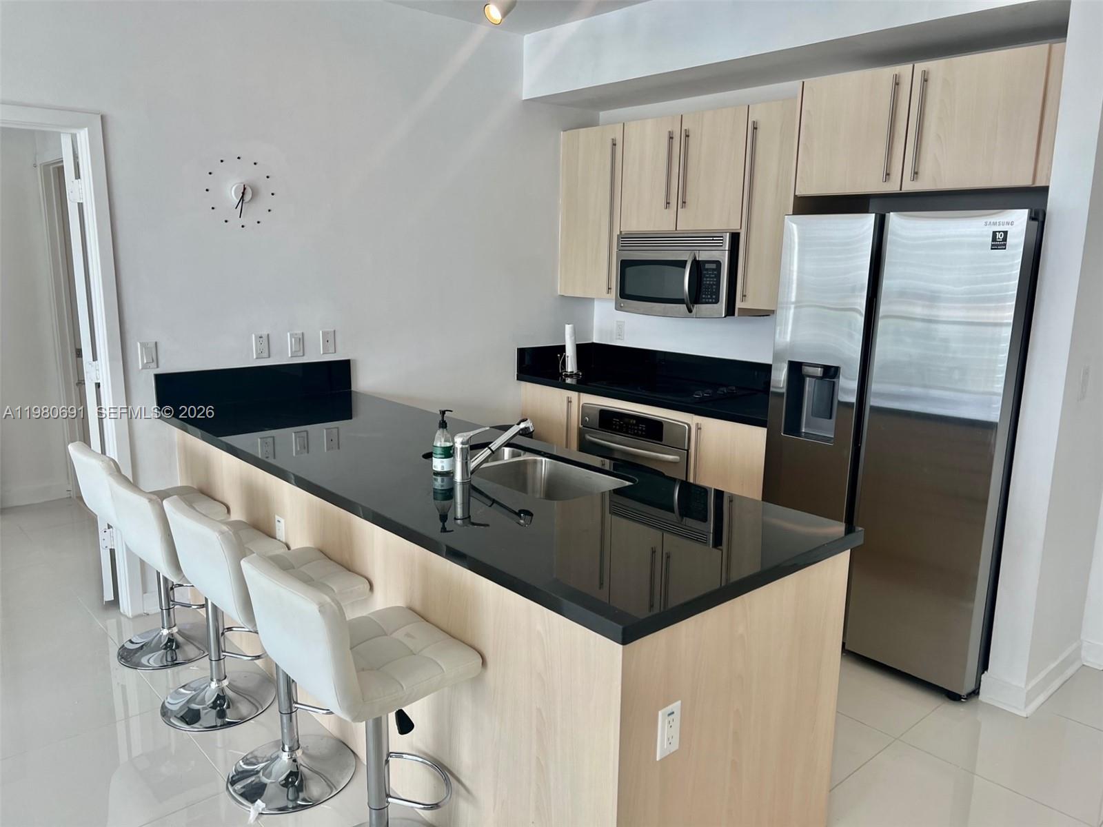 A kitchen features light wood cabinets, black countertops, stainless steel appliances, and three white stools — 1111 SW 1st Ave # 3223, Miami FL 33130, MIAMI, FL