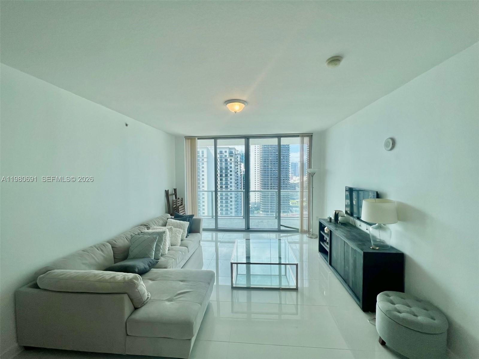 A modern living room features a light gray sectional sofa, glass coffee table, and balcony access — 1111 SW 1st Ave # 3223, Miami FL 33130, MIAMI, FL