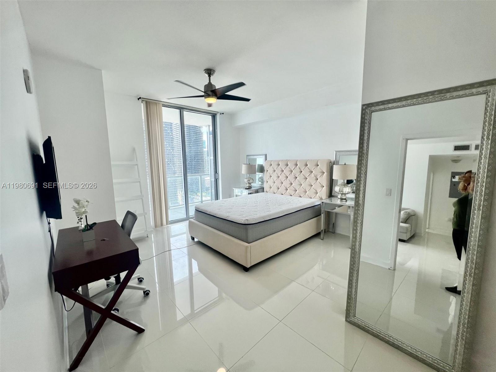 A bedroom features a tufted headboard, white tile floors, a desk, and a large mirror — 1111 SW 1st Ave # 3223, Miami FL 33130, MIAMI, FL