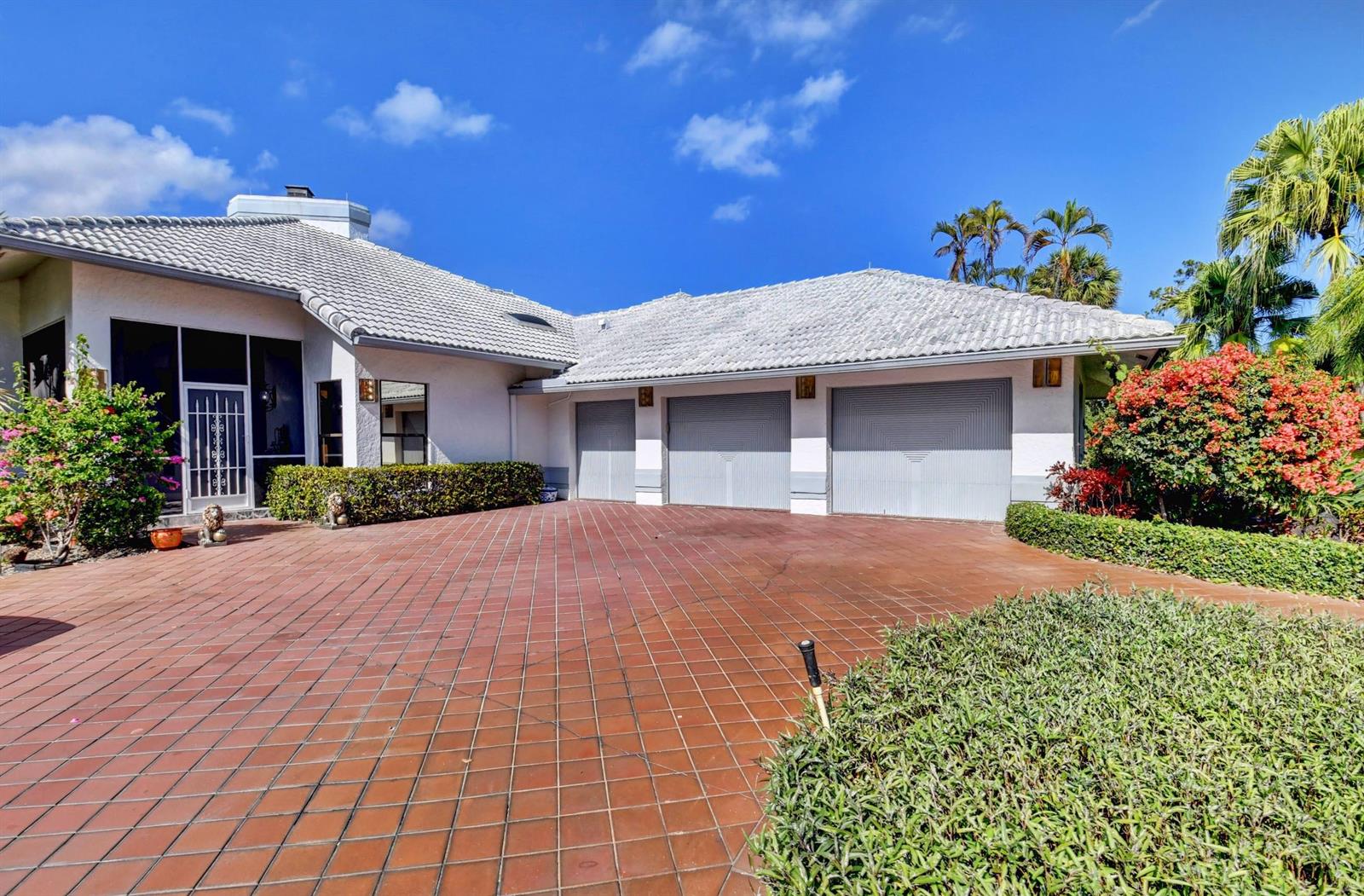 A white house with a three-car garage and a red tiled driveway under a blue sky — 56 Northwoods Lane, Boynton Beach FL 33436, BOYNTON BEACH, FL