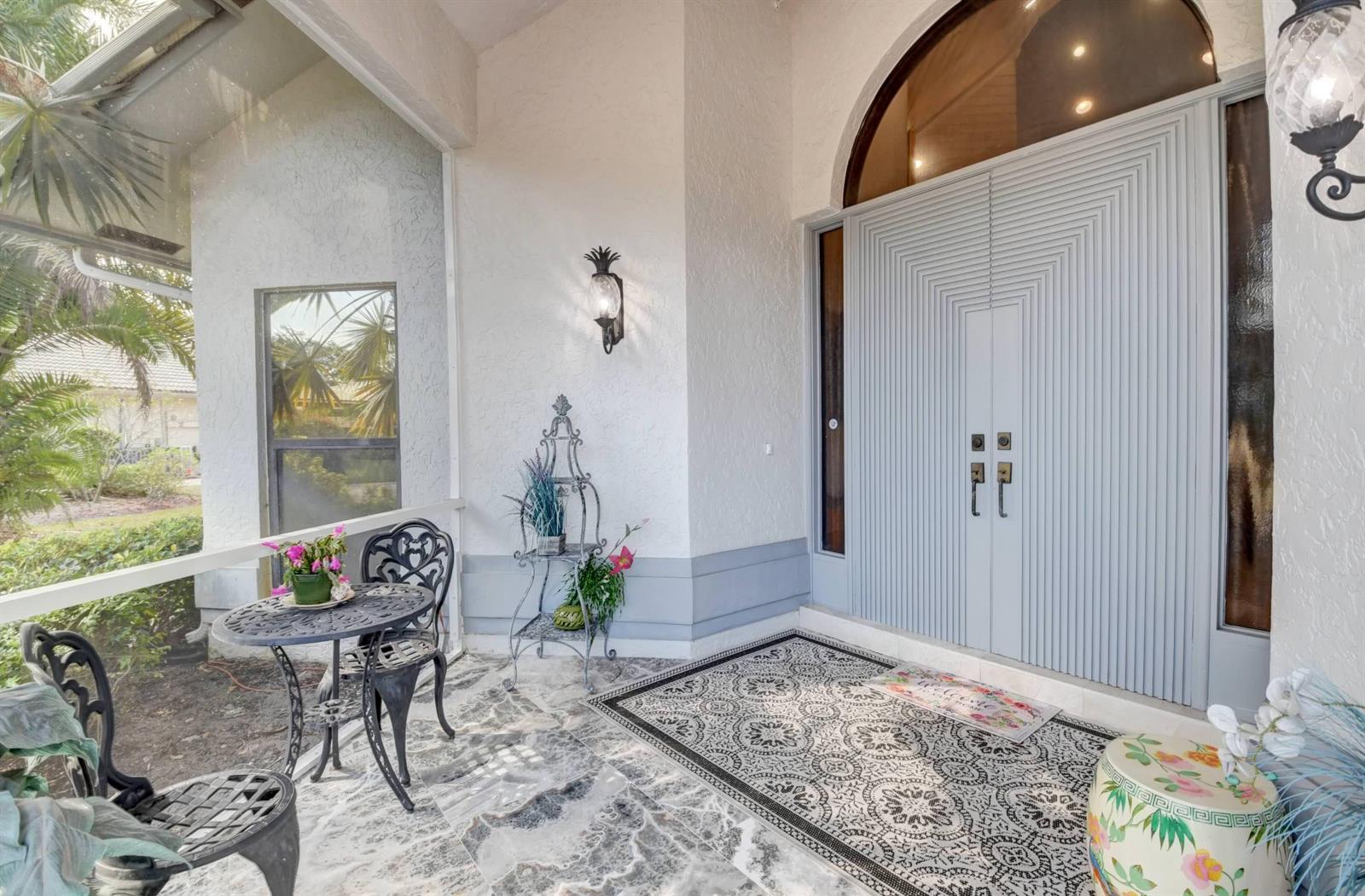 A covered entryway features a double door, marble-look flooring, and a small bistro seating area — 56 Northwoods Lane, Boynton Beach FL 33436, BOYNTON BEACH, FL