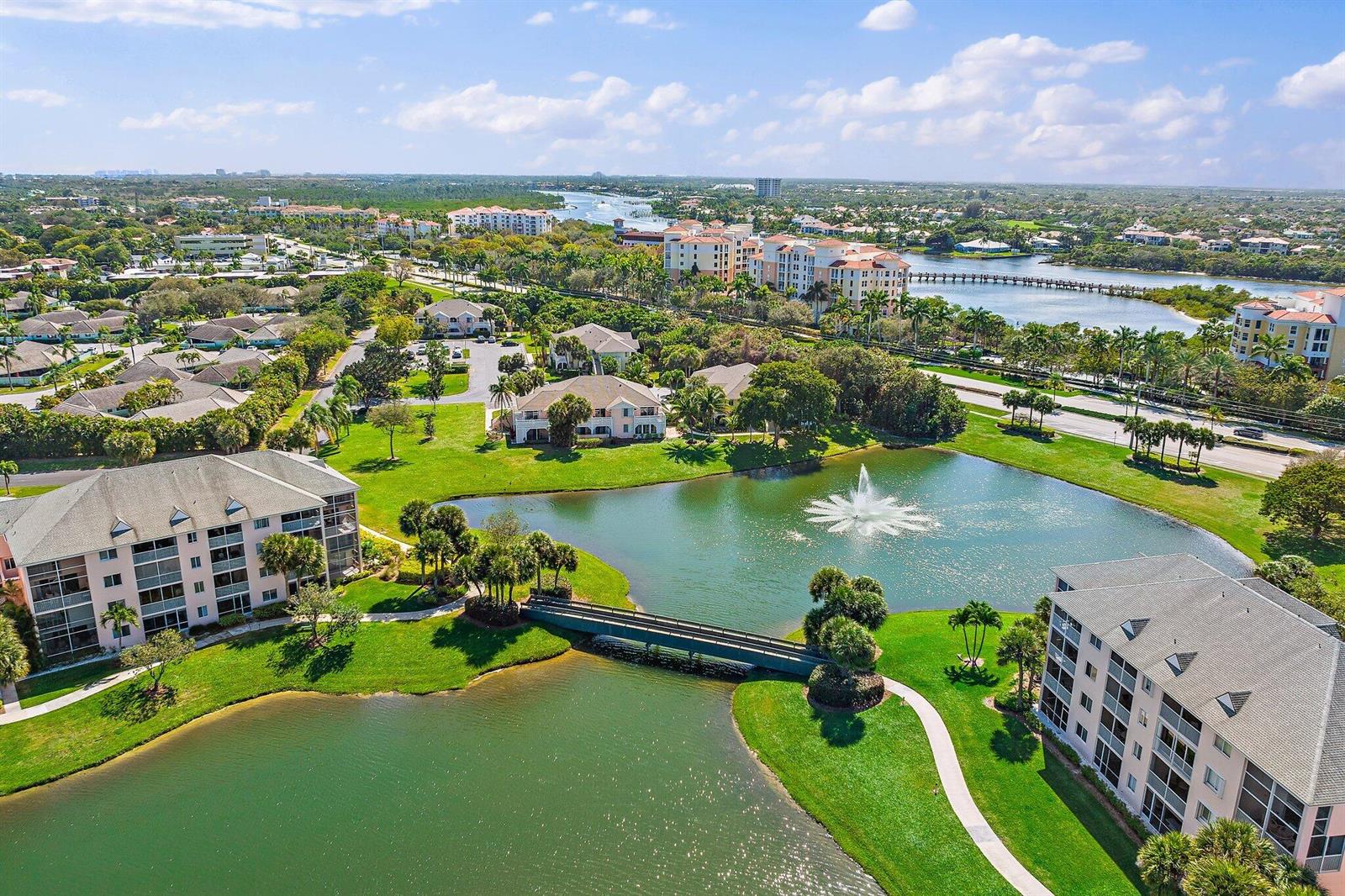 An aerial view of a residential complex featuring a pond, fountain, bridge, and multi-story buildings — 353 S Us Highway 1 # F306, Jupiter FL 33477, JUPITER, FL