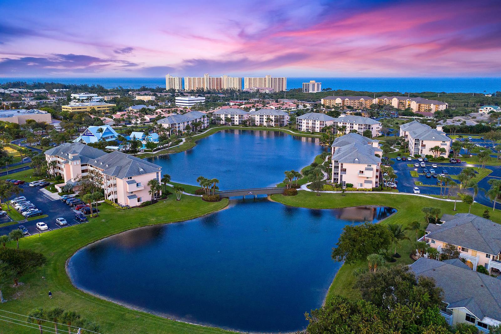 Aerial view of a residential complex with multi-story buildings surrounding a central lake and bridge — 353 S Us Highway 1 # F306, Jupiter FL 33477, JUPITER, FL