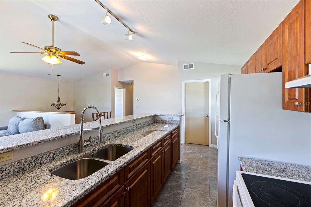 A kitchen features granite countertops, wood cabinets, a double sink, and a view into the living room — 334 CROSSWINDS DRIVE, PALM HARBOR, FL