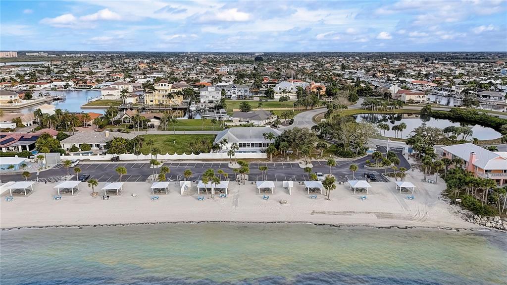 An aerial view shows a sandy beach with shaded seating areas, a parking lot, and houses — 5153 TURQUOISE LANE UNIT 102, NEW PORT RICHEY, FL