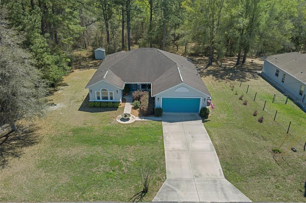 An aerial view shows a single-story house with a blue garage door and a driveway — 8623 N DORA WAY, DUNNELLON, FL