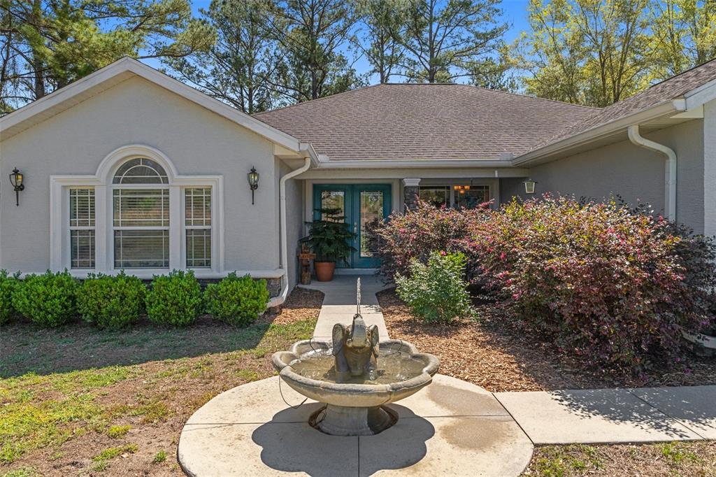 A light-colored house exterior features a front fountain, a walkway, and double entry doors — 8623 N DORA WAY, DUNNELLON, FL