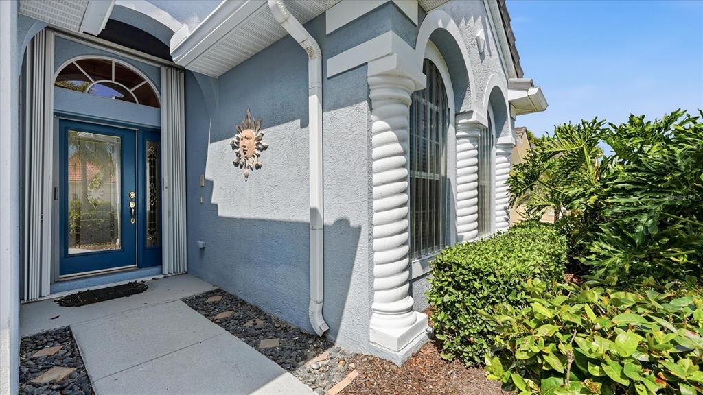 The exterior of a blue house features a glass-paneled front door and decorative columns — 5704 WHITE JASMINE WAY, NORTH PORT, FL