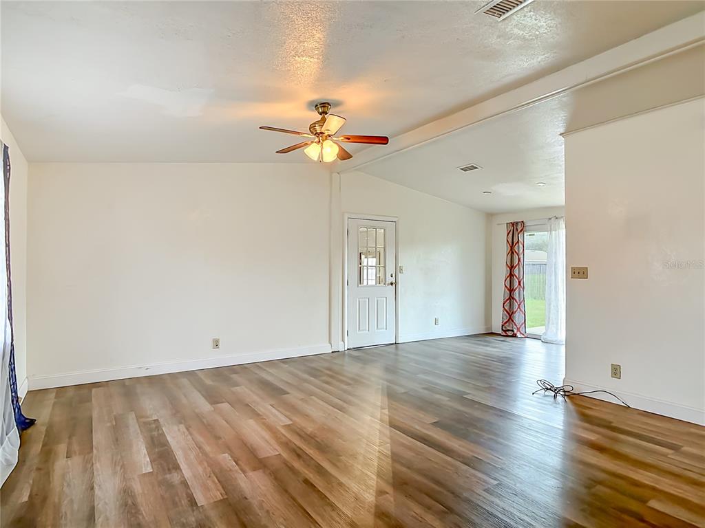 An empty living room features wood-look flooring, a ceiling fan, and a glass-paneled exterior door — 943 MONROE HARBOR PLACE, SANFORD, FL