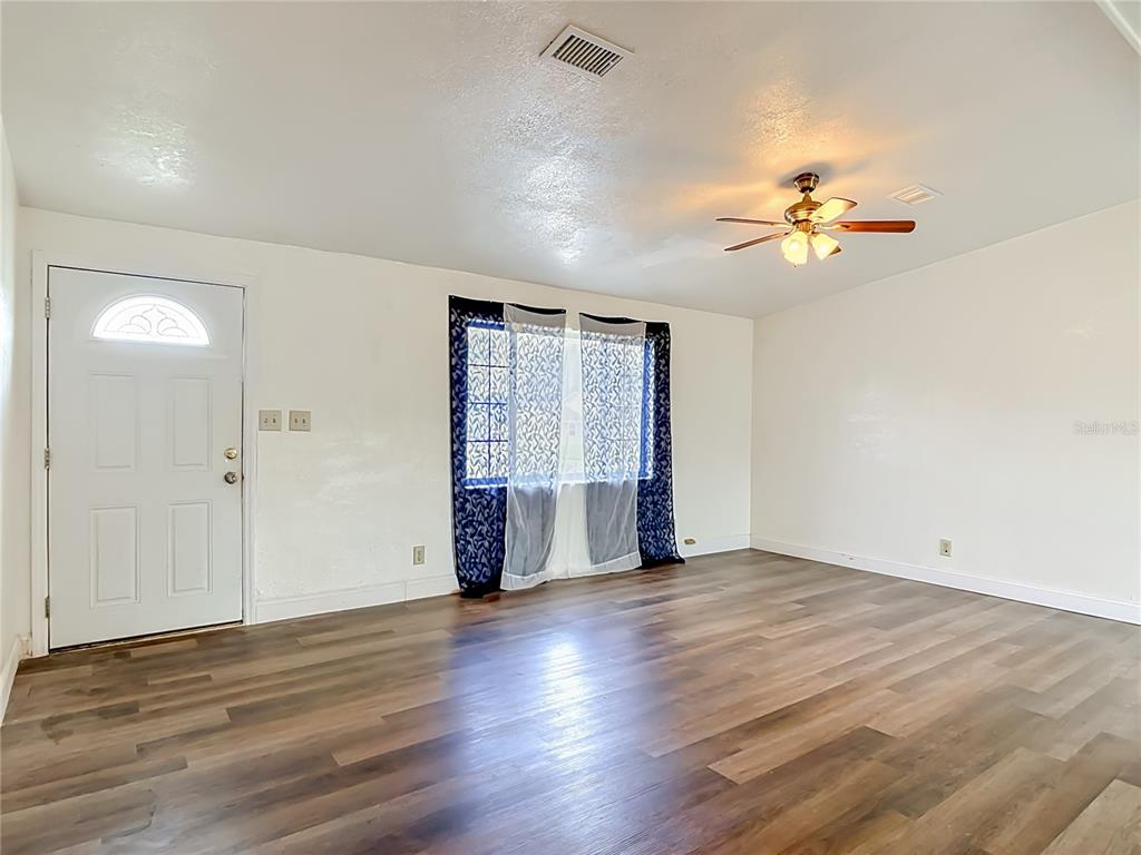 An empty living room features wood-look flooring, white walls, a ceiling fan, and a front door — 943 MONROE HARBOR PLACE, SANFORD, FL