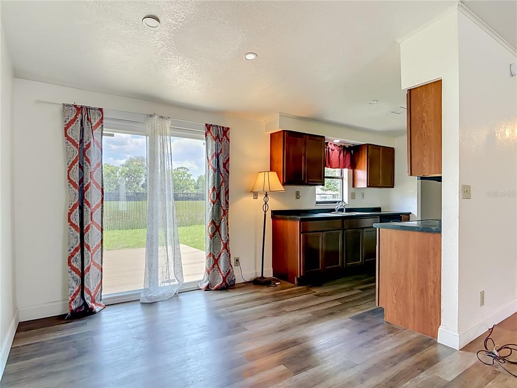 A kitchen with dark wood cabinets and wood-look flooring opens to a sliding glass door — 943 MONROE HARBOR PLACE, SANFORD, FL