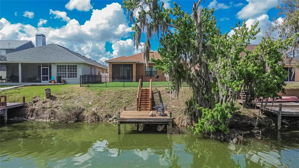 A wooden dock with stairs leads up a grassy bank to two houses by water — 6870 SHIMMERING DRIVE, LAKELAND, FL