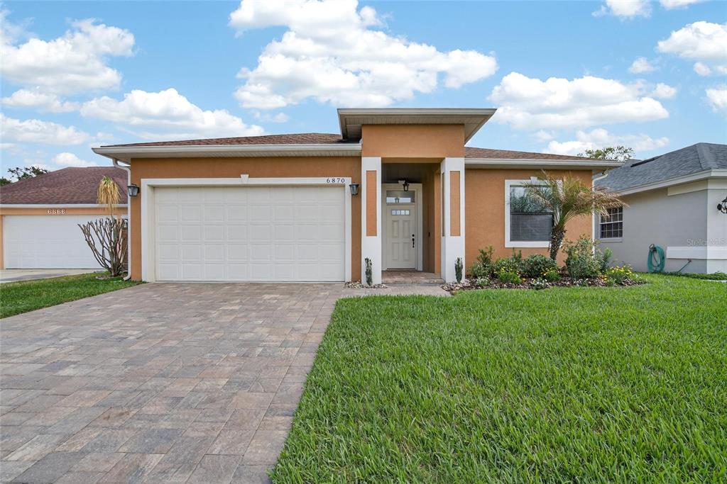 A single-story house with a tan stucco exterior, a paved driveway, and a two-car garage — 6870 SHIMMERING DRIVE, LAKELAND, FL